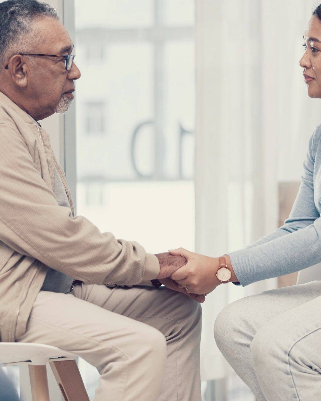A caregiver and a family member sitting together holding hands